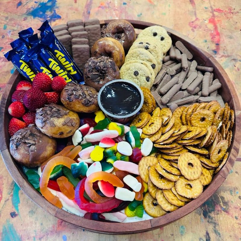 DIY Invasion's catering called sweets platter with assorted snacks including cookies, candies, and crackers on a wooden tray.